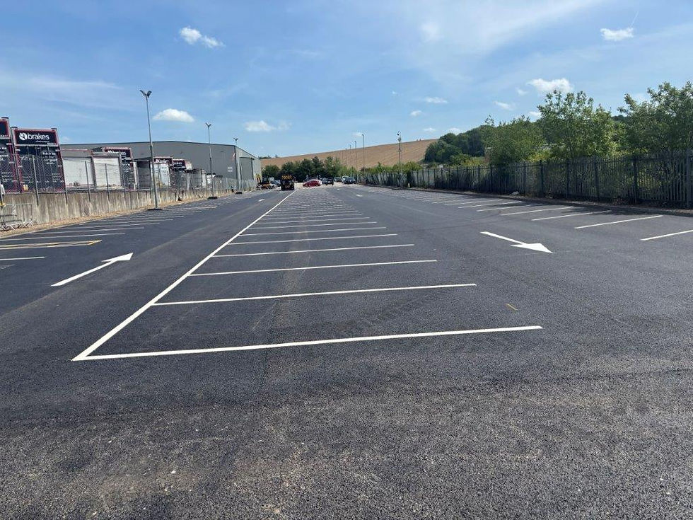 Kerbside view of an empty car park with a drainage grate and landscaped greenery on the left.