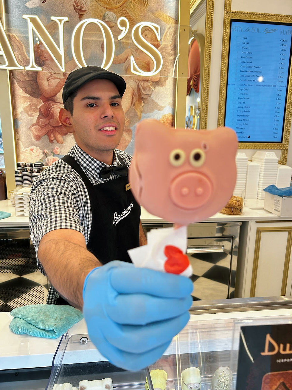 Empleado de heladería Lucianos sonríe y ofrece un helado de cerdito; fondo con menú azul y decoración dorada.