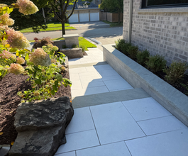Horvath Landscaping front walkway with large-format concrete pavers, clean joints, and a natural stone retaining wall edge.