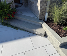 Horvath Landscaping front entry detail featuring modern pavers, a concrete step landing, and a raised planter wall with ornamental grasses.