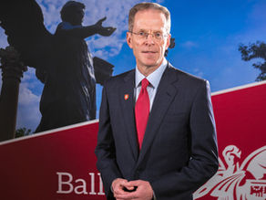Ball State University President Geoffrey Mearns stands in front of a Ball State banner showing the Beneficence statue