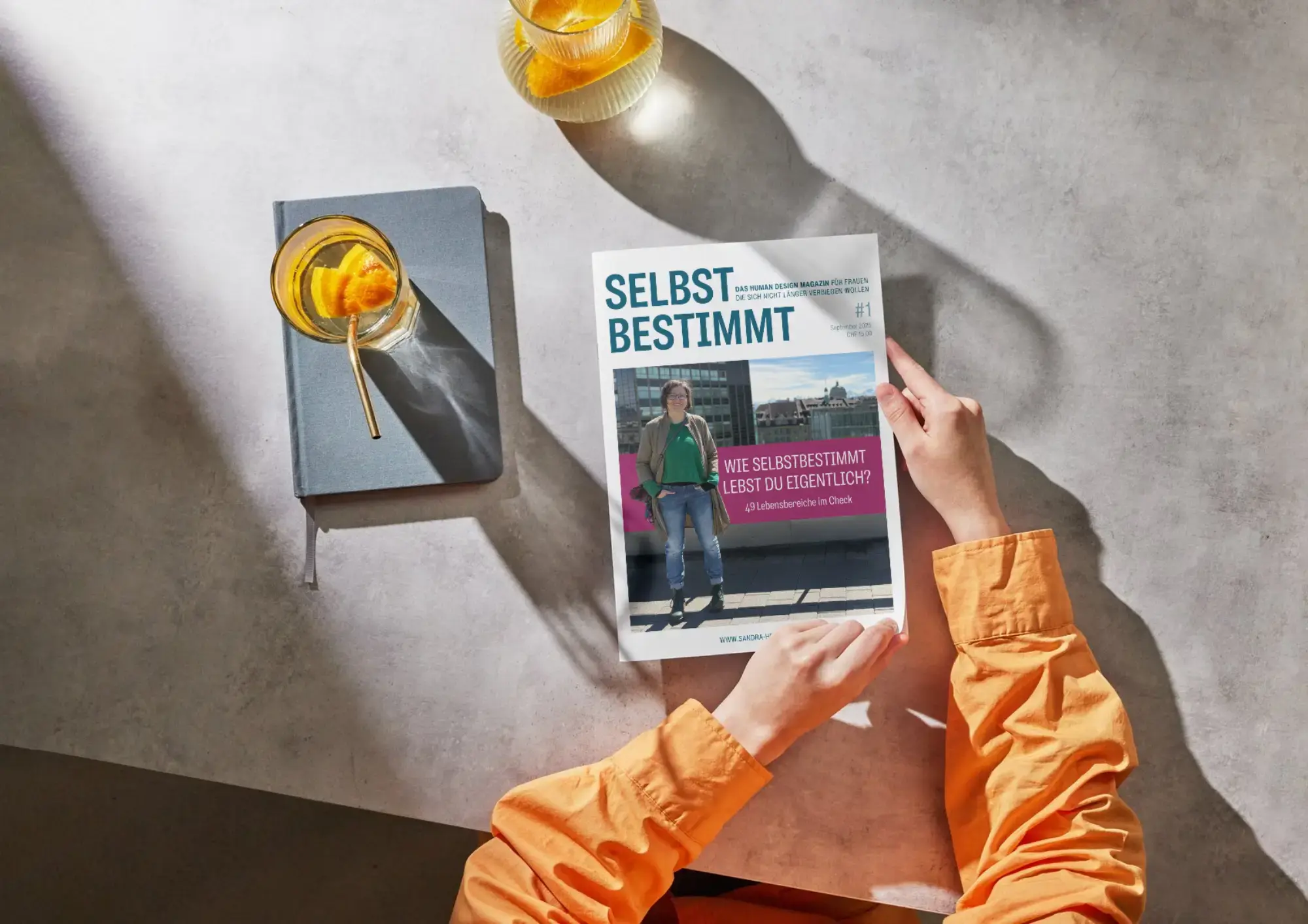 Printversion des Human Design Magazins von Sandra Hoppenz auf einem Schreibtisch. Eine Frau in einem orangenen Hemd blättert