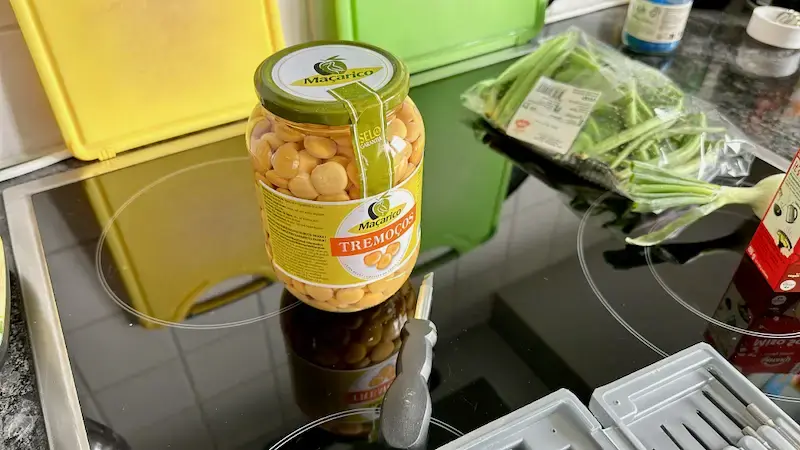 Ein Glas Tremocços mit dem Label "Macarico" steht auf einem schwarzen Kochfeld.Ein Glas Tremocços steht auf einem schwarzen Kochfeld. Ein Schraubendreher liegt für das Öffnen bereit