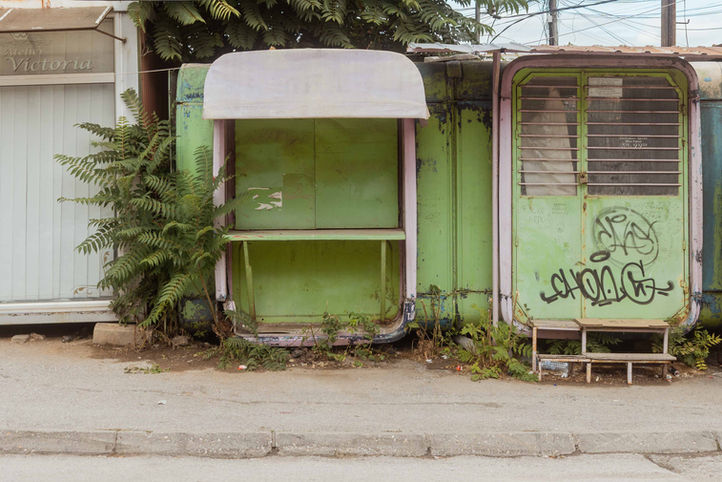 Abandoned green kiosk overgrown with ferns and plants — urban photograph from the series Absent Presences by Czech photographer Aneta Ježková, exploring the gentle reclaiming of human spaces by nature.