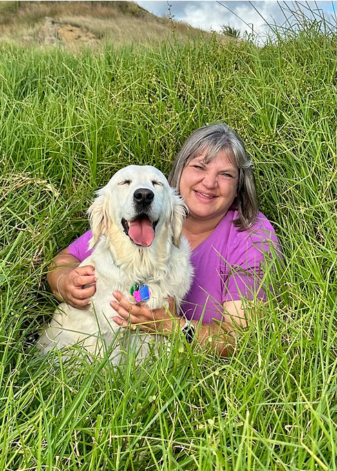Photo of assistance dog Addie, a white golden retriever, with her owner Belinda sitting in long grass.