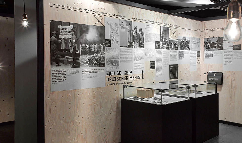 Eine Plaktwand in der Sonderausstellung Fremde Heimat, die mit Texten beklebt sind und von der Flucht der Familie Mann vor dem Krieg erzählen.