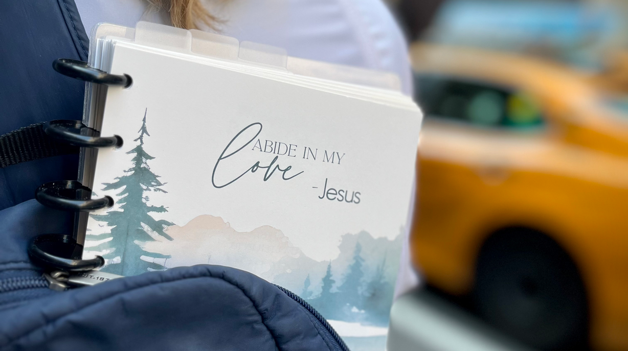 An Abiding in Jesus Day Planner peeking out of a backpack in a city setting.