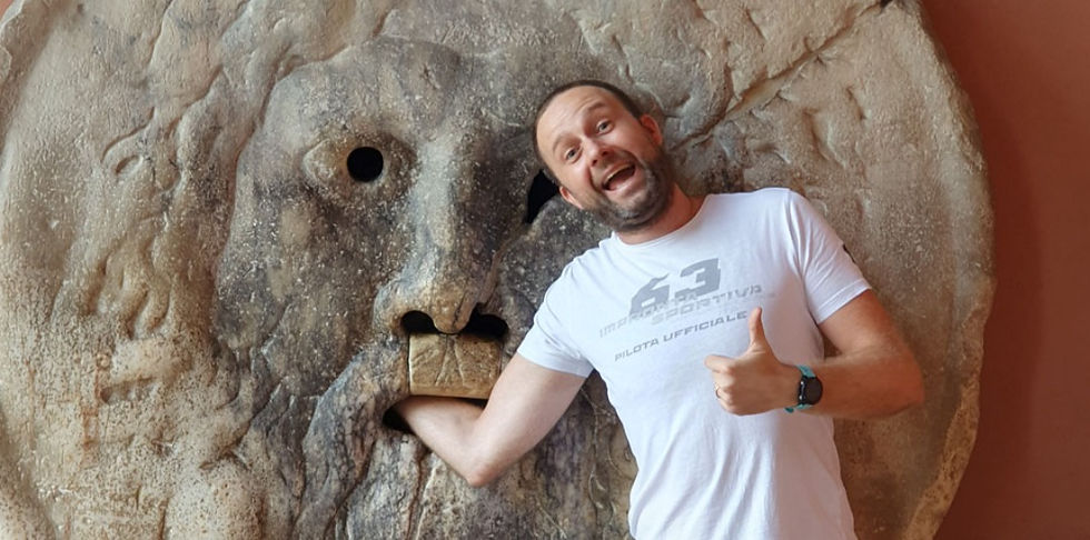 Um homem sorridente com uma camiseta branca colocando sua mão dentro da famosa Bocca della Verità, um antigo mármore mascarão de pavimento de fonte, em Roma.