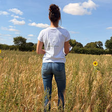 A person standing in a green field, bright blue sky and sunshine
