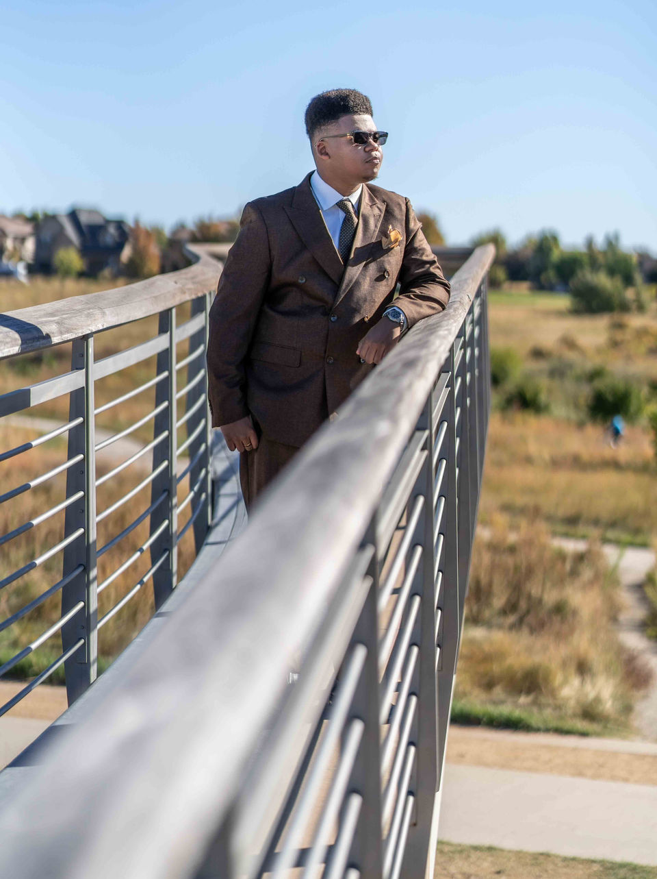 Man in brown suit and sunglasses, leaning on a bridge, LW Productions.