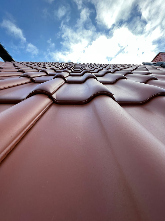 Rot engobierte Röben-Tondachziegel, fotografiert von der Traufe in Richtung First, Nahaufnahme einer gedeckten Dachfläche.