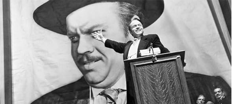 Citizen Kane (Orson Welles) campaigns for governor in front of a massive poster of himself, signifying his inflated ego and ambition. Image courtesy of IMDb.com.
