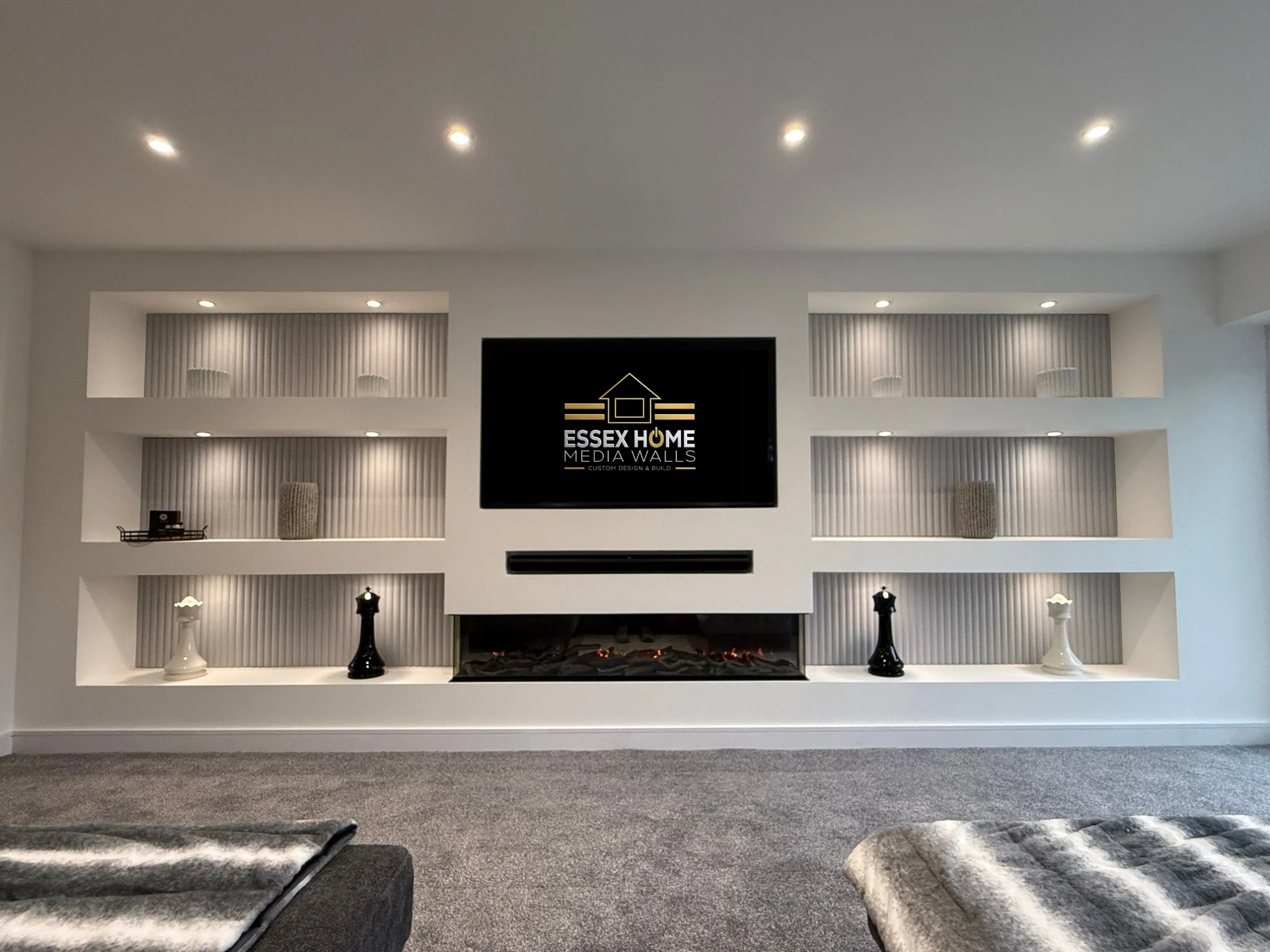 White media wall with six ribbed display niches, spotlights, a recessed TV and electric fire
