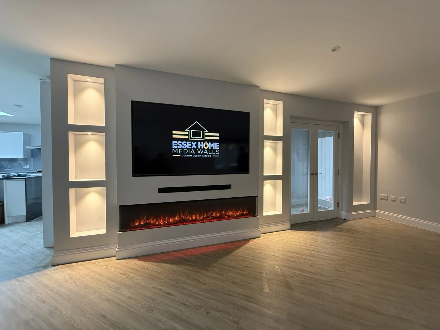 Media wall with a wide electric fire and lit display niches beside glazed doors