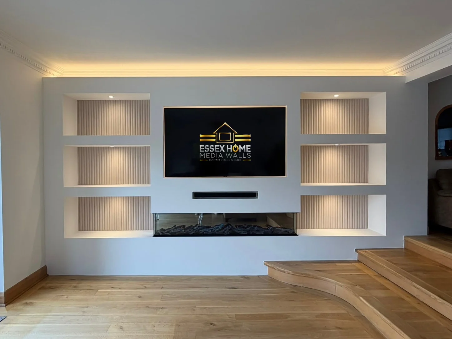 Media wall with six lit niches and ceiling lighting beside timber steps