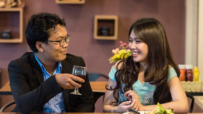 Man and woman smiling at each other in a cozy restaurant. The man holds a wine glass. A plate of food is on the table. Warm atmosphere.