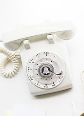 A telephone. The phone is vintage ins style, perhaps from the early eighties with a rotary mechanism for dialling. It appears hard and white and is on a white background.