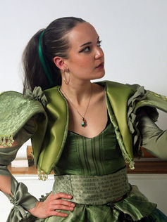 As one of the sisters. Elsie has an animal she dresses up as: a frog. Her favourite items to collect are flowers. The crinoline represents the frog`s round shape, while her fabric is printed frog skin. The prophecy “murderer, martyr, monarch, mad” is flocked, embroidered, and printed onto all the sisters` costume, as they write it everywhere. She has gloves to simulate a frog`s palm while her bodice has laser cut circles in the shape of a frog`s skin on the back. The top layer of her skirt is an x ray print and she has an x ray of a frog embroidered on her chest.