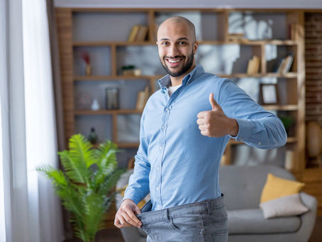 Smiling man giving a thumbs up while showing loose-fitting jeans after successful weight loss