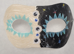 Three dimensional black and white mask. The left side painted in white, using white yarn to connect to the center of the mask to a gem then back around following the contour of the mask until the left space The right side is painted black and adorned with stars. The inside of the open eyes are painted with connected blue triangles all the way around.