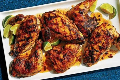 Grilled jerk chicken pieces served on a white platter with lime wedges.