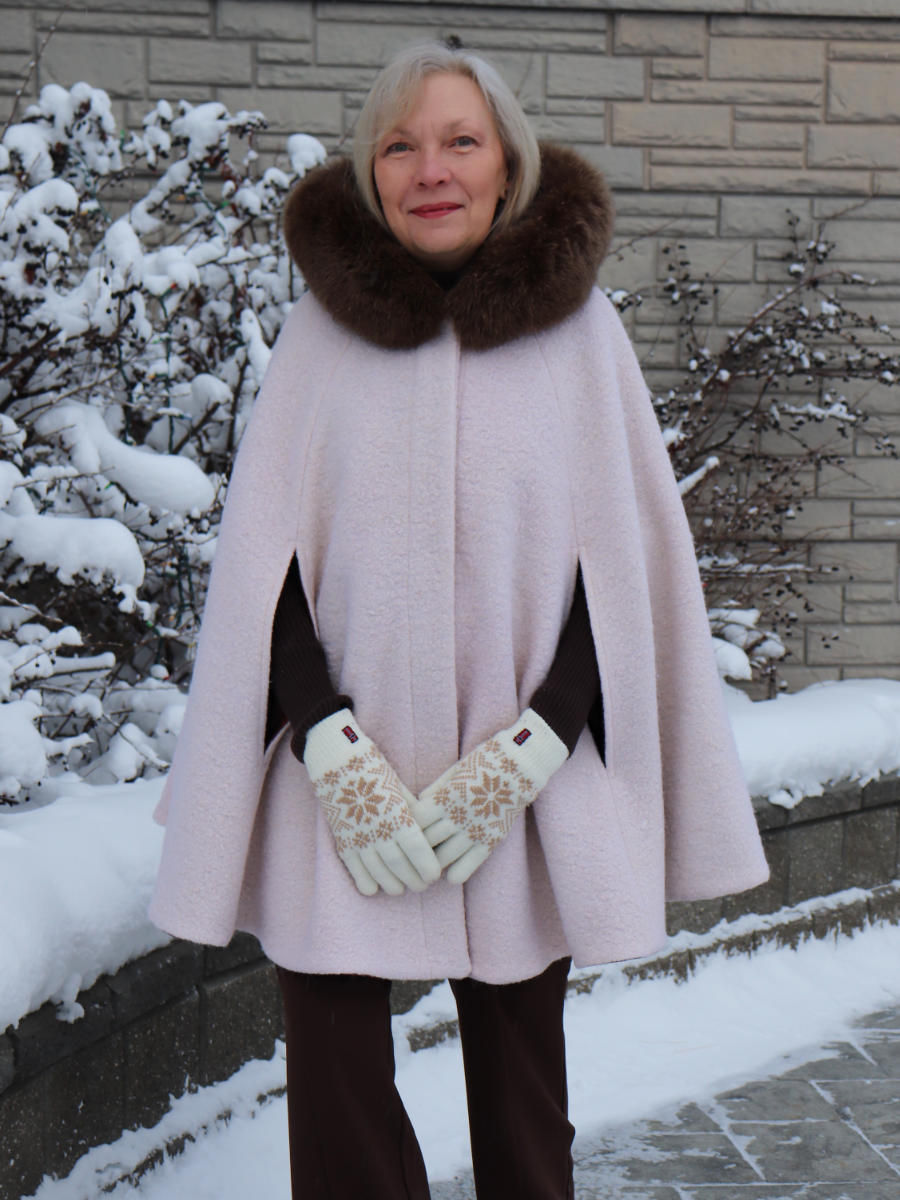 A woman wearing an elegant, cream coloured cape with brown fur around the hood. The hood is down.