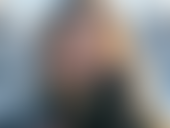 Primer plano de una mujer sonriente protegiéndose del frío invernal con una bufanda gruesa de cuadros y guantes de lana, con escarcha visible en su cabello y pestañas en un paisaje nevado.