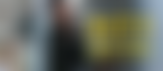 Noah Wyle in a hospital leaning against the glass door. The Pitt logo is on the right. 