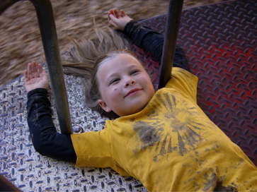 A young girl lies on her back on a Merry-Go-Round. She is smiling and looking up at the sky.