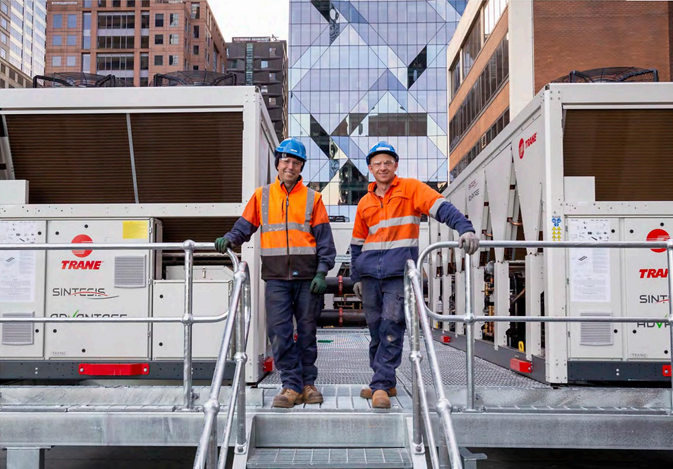 Two men in high-vis standing in front of Trane heat pumps on the 101 Collins office building