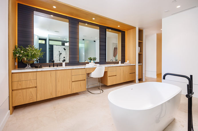 Modern master bathroom with a freestanding bathtub, a walk-in shower with a glass enclosure, two vanities with modern fixtures, and a window. Real estate photography by Adam Dubich Photography, Orange County, California