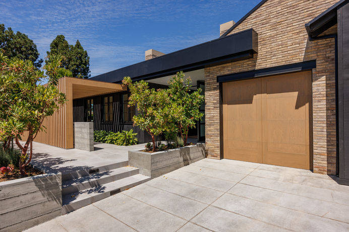 View of a modern house with a wooden garage door from the driveway. The house is located in a residential neighborhood in Orange County, California. Real estate photography by Adam Dubich Photography.