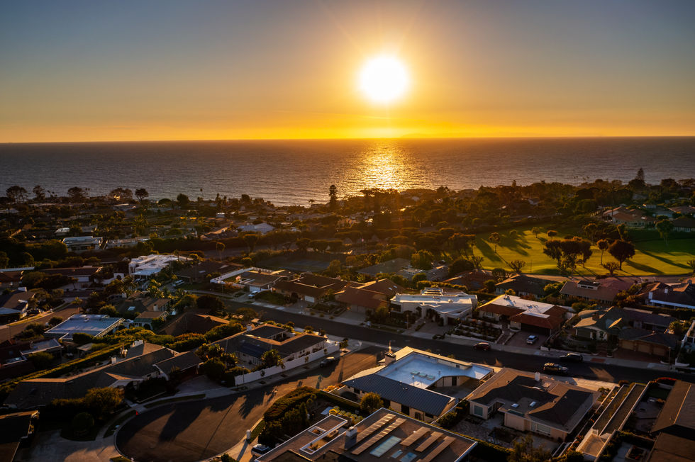 an aerial view of a residential area with the sun setting over the ocean