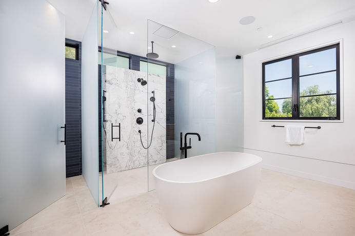 Master bathroom with a freestanding bathtub, a walk-in shower with frosted glass enclosure, and modern fixtures. Real estate photography by Adam Dubich Photography, Orange County, California.