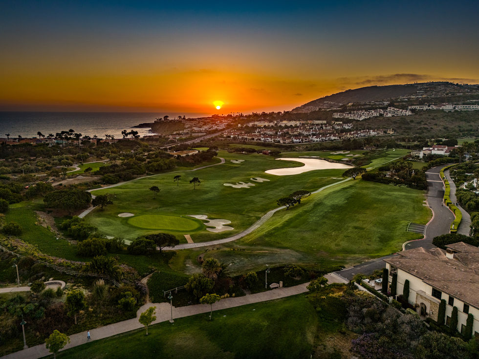 an aerial view of a golf course with the sun setting in the background