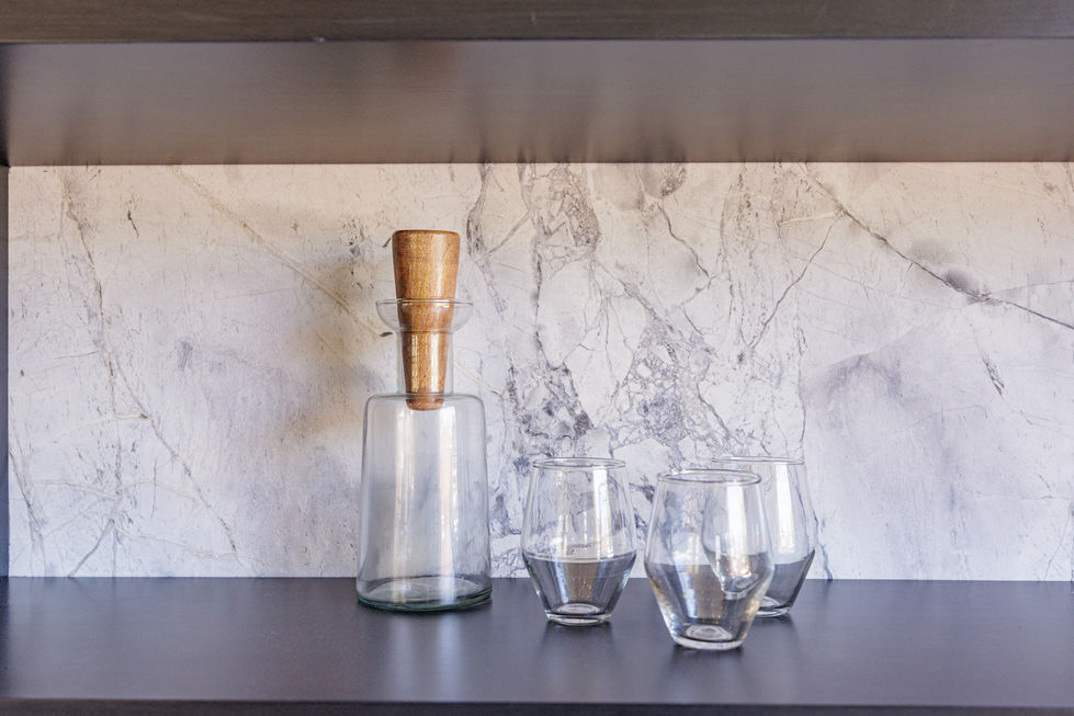 a glass bottle with a wooden handle sits on a shelf next to three empty glasses