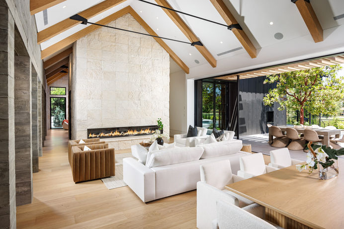 Living room with a modern fireplace, couch, armchair, coffee table, and woven rug. Large windows fill the space with natural light. Real estate photography by Adam Dubich Photography, Orange County, California.