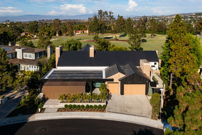 Aerial view of a modern house in Orange County, California. The house has a black roof with solar panels and is surrounded by trees. Real estate photography by Adam Dubich Photography.