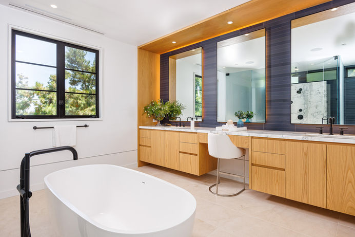 Modern master bathroom with a freestanding bathtub, a walk-in shower with a glass enclosure, two vanities with modern fixtures, and a window. Real estate photography by Adam Dubich Photography, Orange County, California