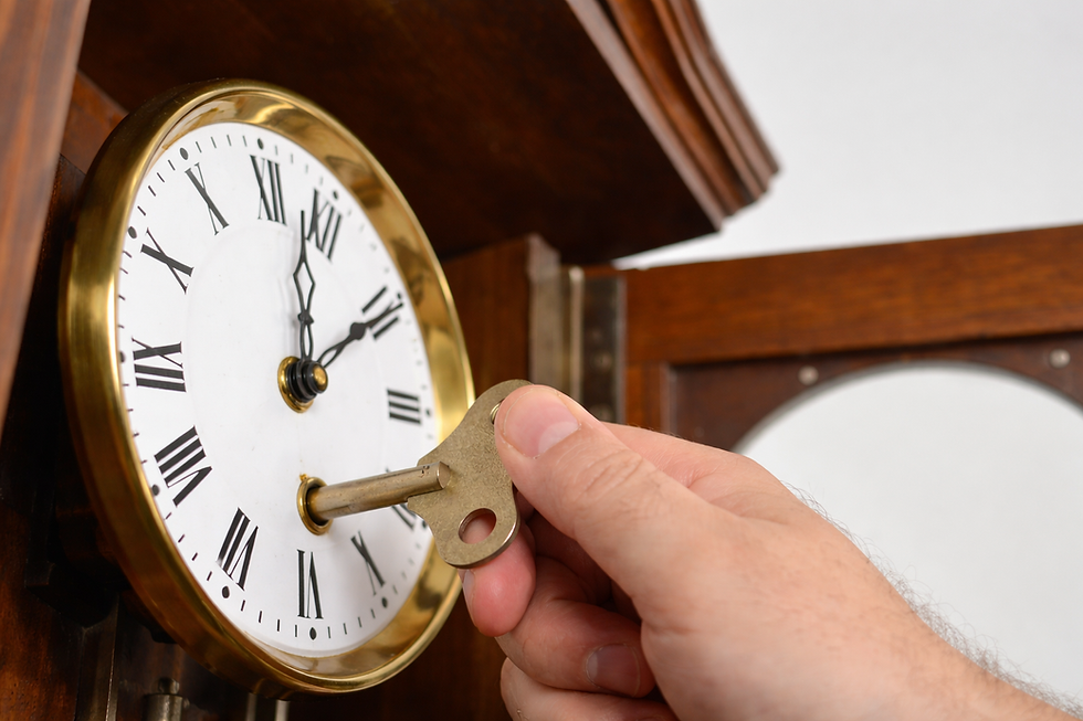 Hand winding a vintage clock with a brass key. The clock face shows Roman numerals. Wooden casing in the background.
