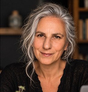 Nina Roosen mit locker zurückgenommenen silbernen Haaren am Schreibtisch mit Laptop und Büchern.