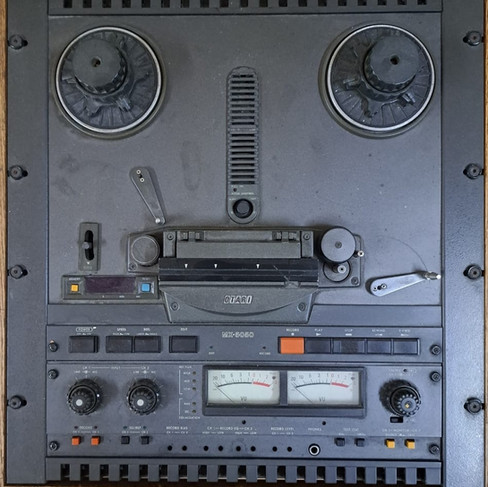 Close-up of a black reel-to-reel machine with dials and control buttons, placed on a wooden surface.