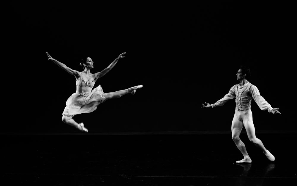 Two ballet dancers captured in a breathtaking grand jeté on a dark stage