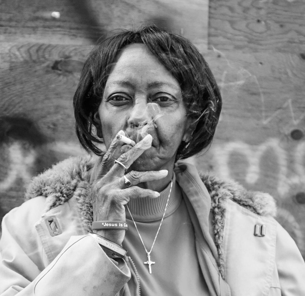 Woman holding a cigarette to her lips, wearing a small cross necklace