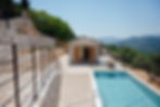 High-angle view of the villa estate showing the stone retaining wall, parking area, private swimming pool, outdoor dining terrace, and scenic valley background.