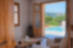 View through open wooden french doors from a modern living room out to a private swimming pool terrace and mountain backdrop.