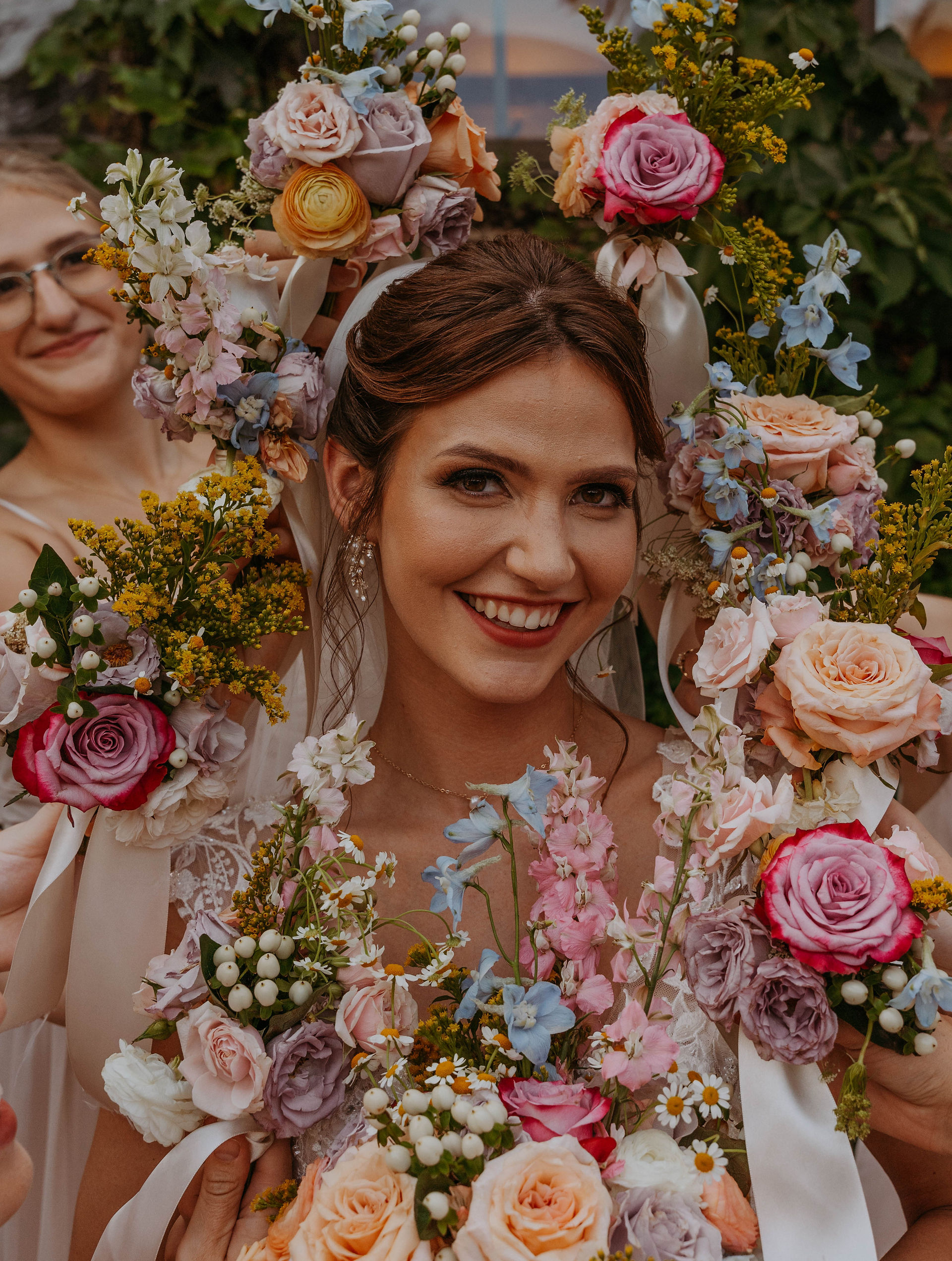 Bride's face is centered as bridesmaids hold their flower bouquets around her face for an editorial bridal portrait.