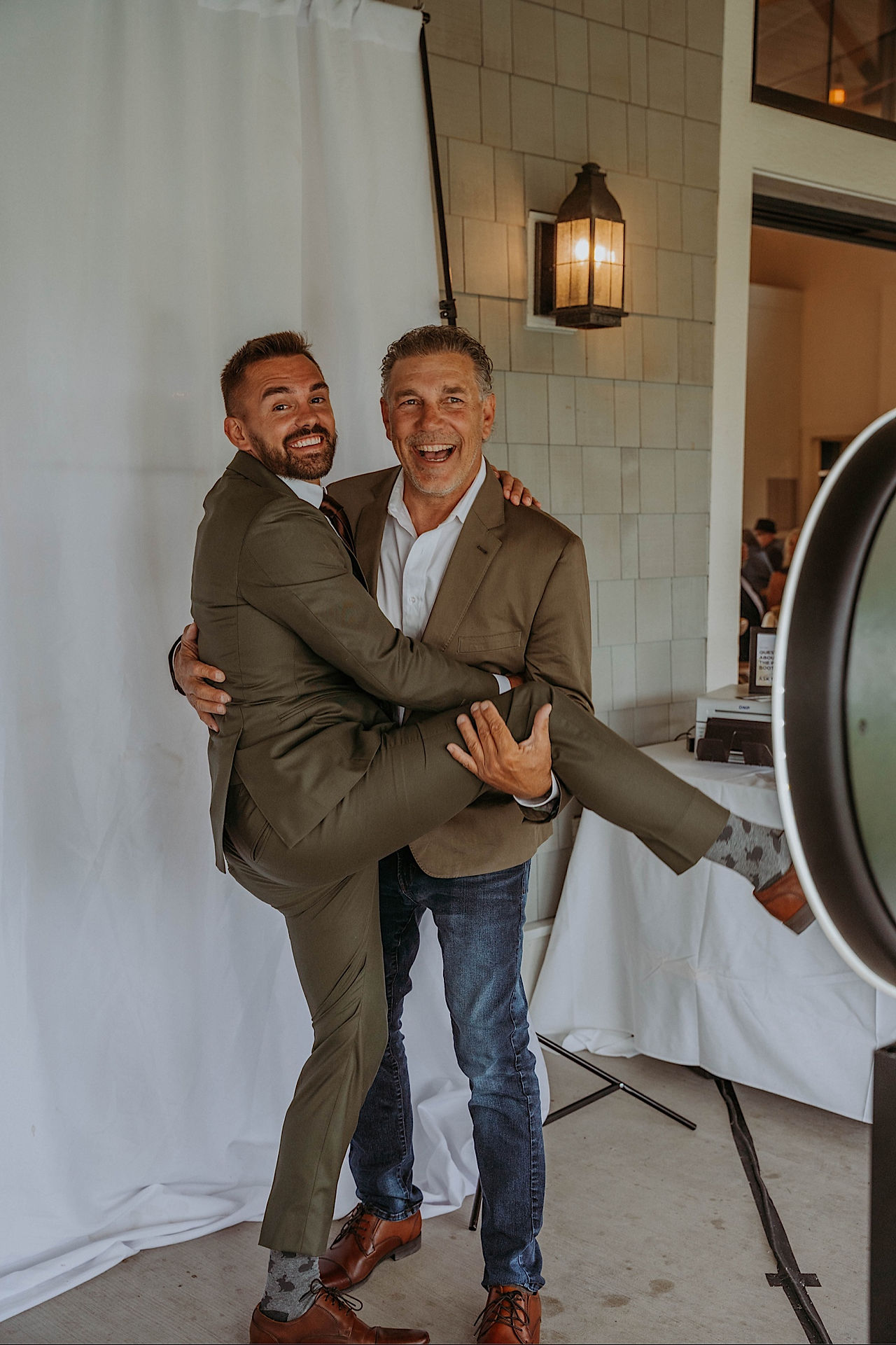 Groom's father holds his leg as they hug while waiting behind a curtain. 