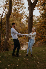 Newly engaged couple taking photos at a forest preserve during the fall months, where the the tree colors are bright orange and yellow