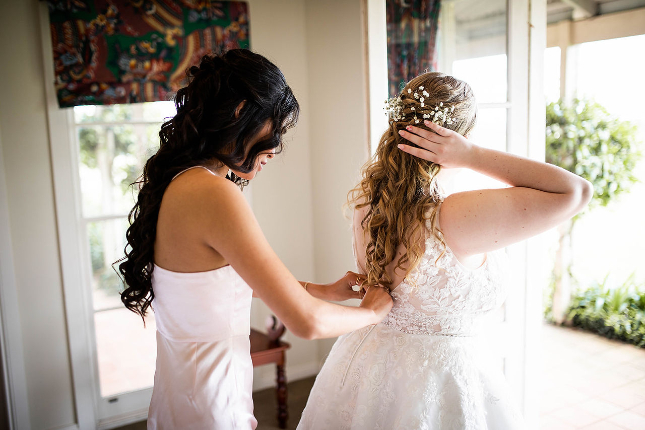 Bridesmaid helps bride with Dress
